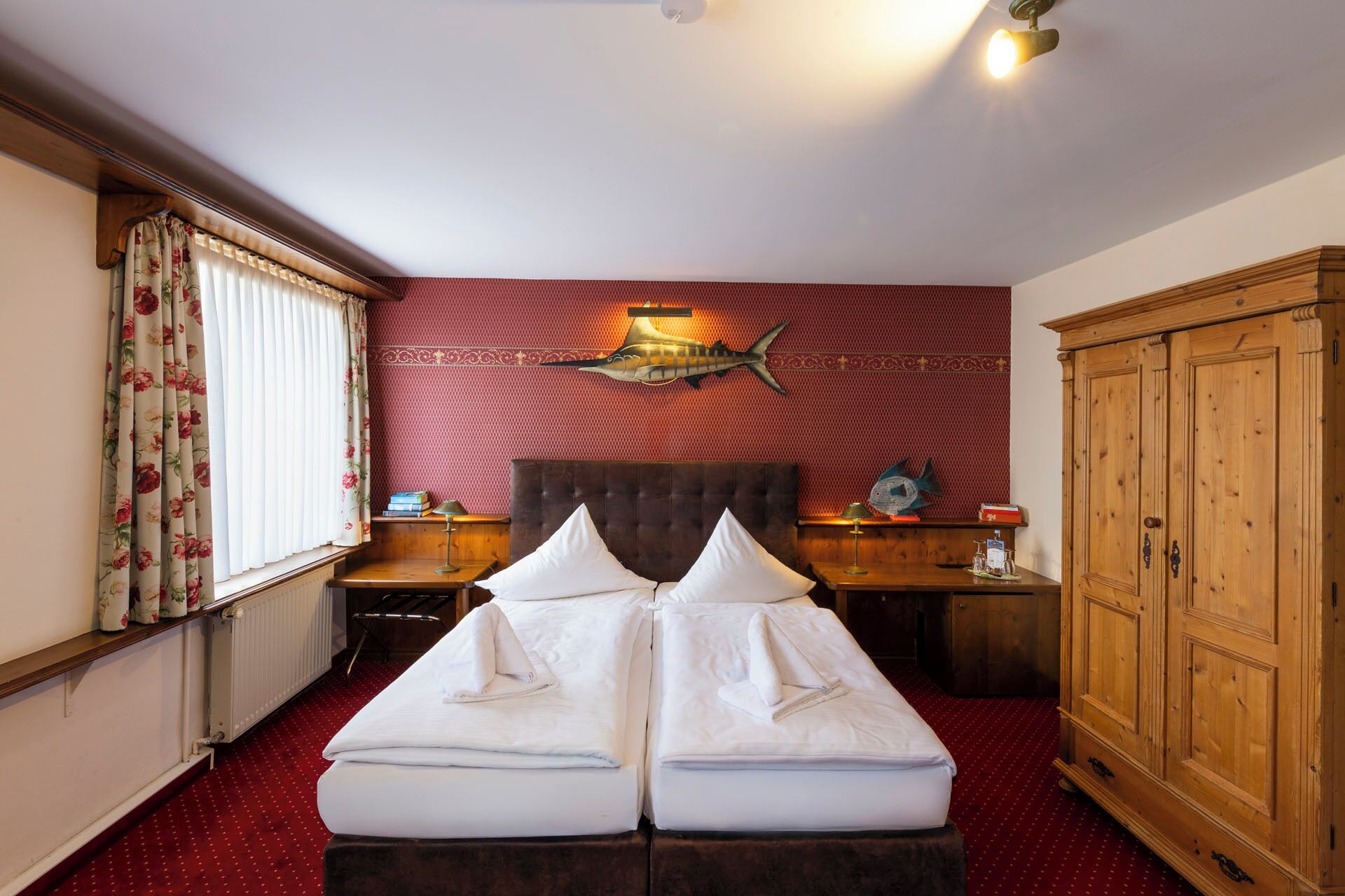 Habitación de hotel con cama doble, armario de madera y pared con estampado rojo.