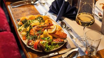 A dining table with a variety of seafood and vegetables, a glass of white wine, and dining utensils.