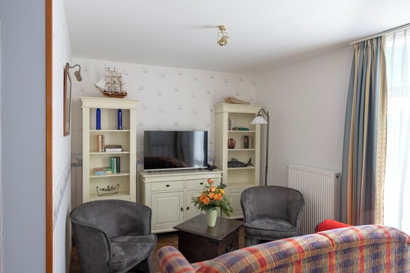 A living room with a TV, two armchairs, a sofa, and a cabinet with decorative items.