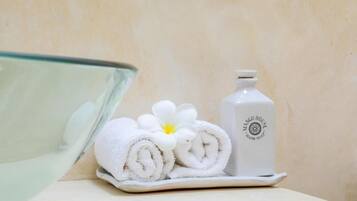 A bathroom with a glass shower, a white towel with a flower, and a bottle of hand soap.