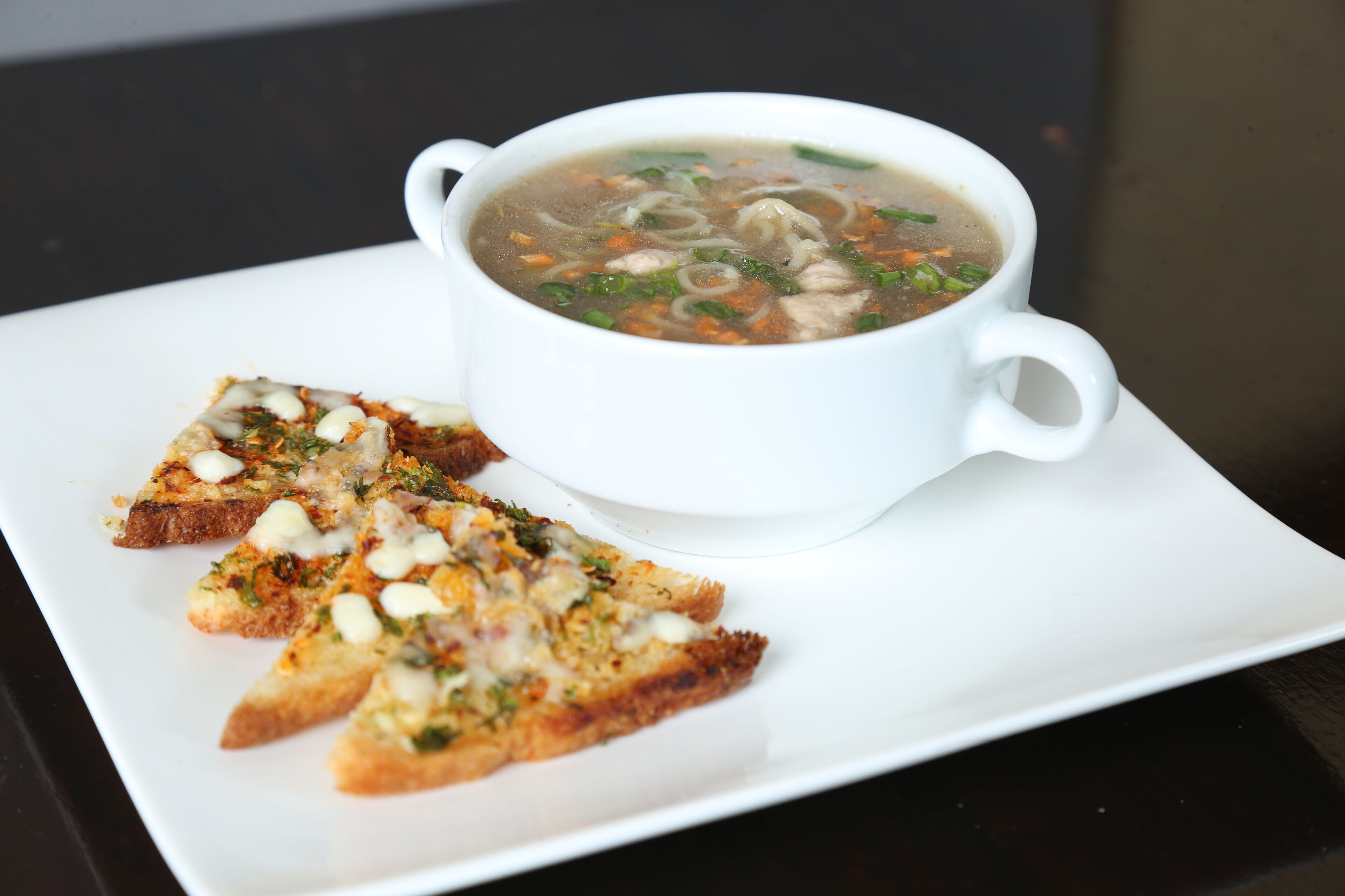En hvid skål suppe med nudler og grøntsager, serveret med en skive ristet brød med fyld.