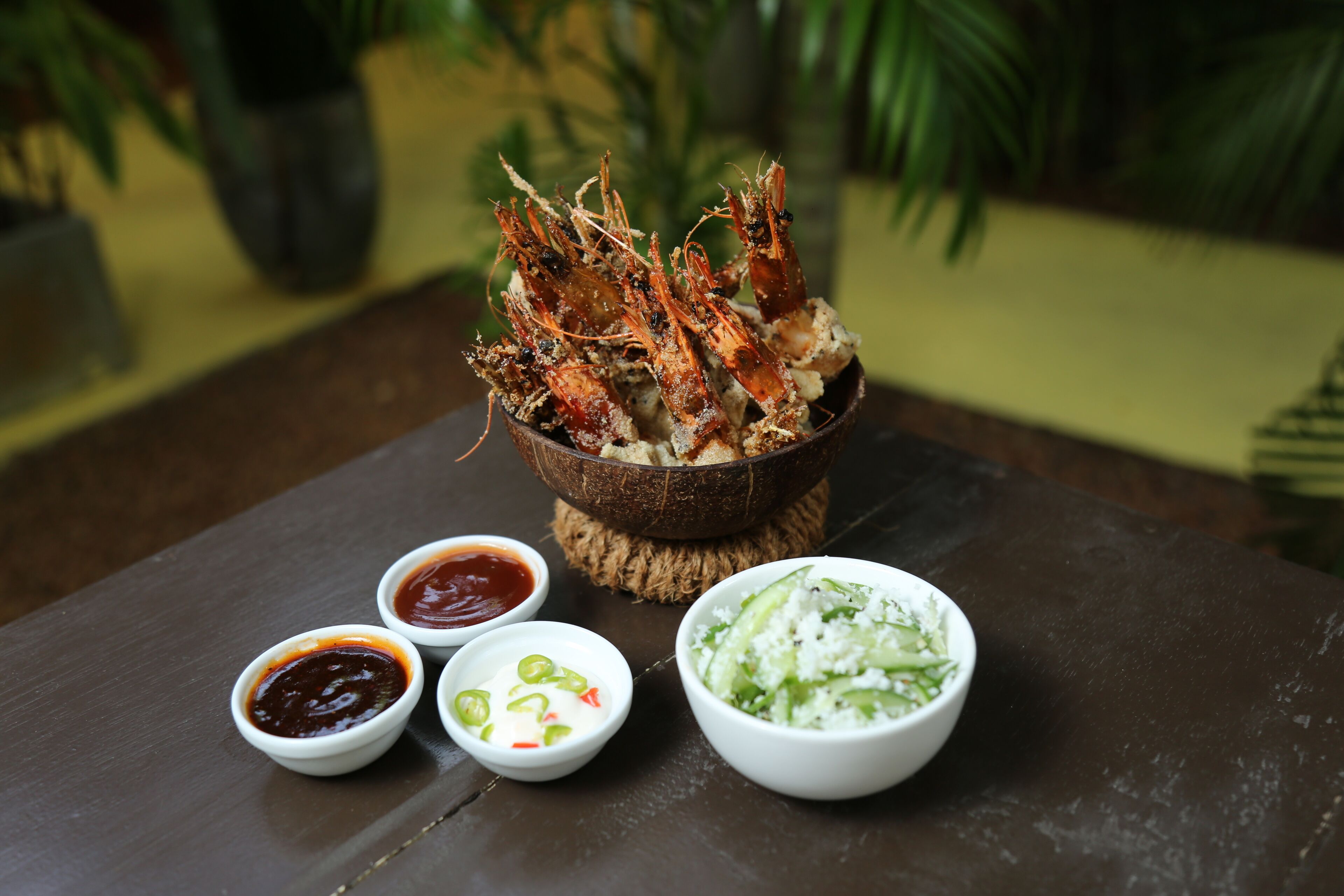 A table with a bowl of cooked shrimp, two small bowls of dipping sauces, and a bowl of salad.