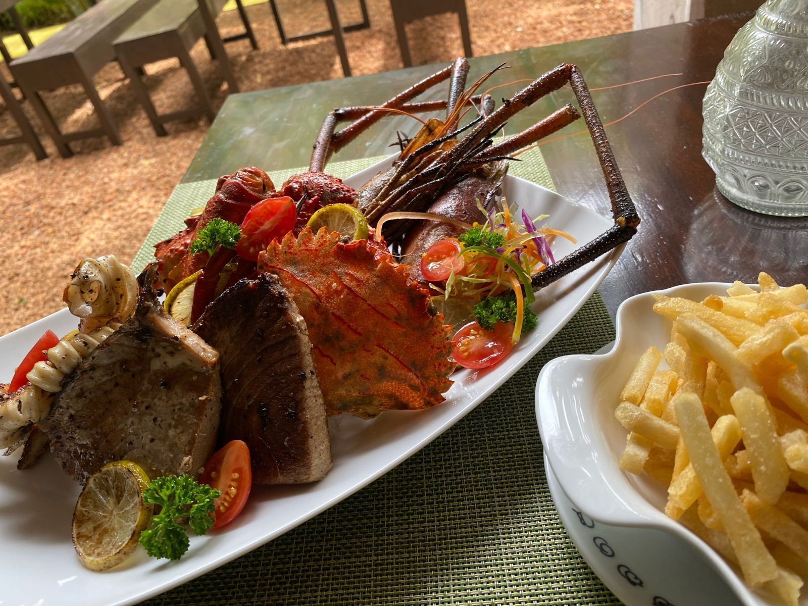 Un plateau de fruits de mer comprenant du homard, des crevettes et un steak, accompagné d’une portion de frites.