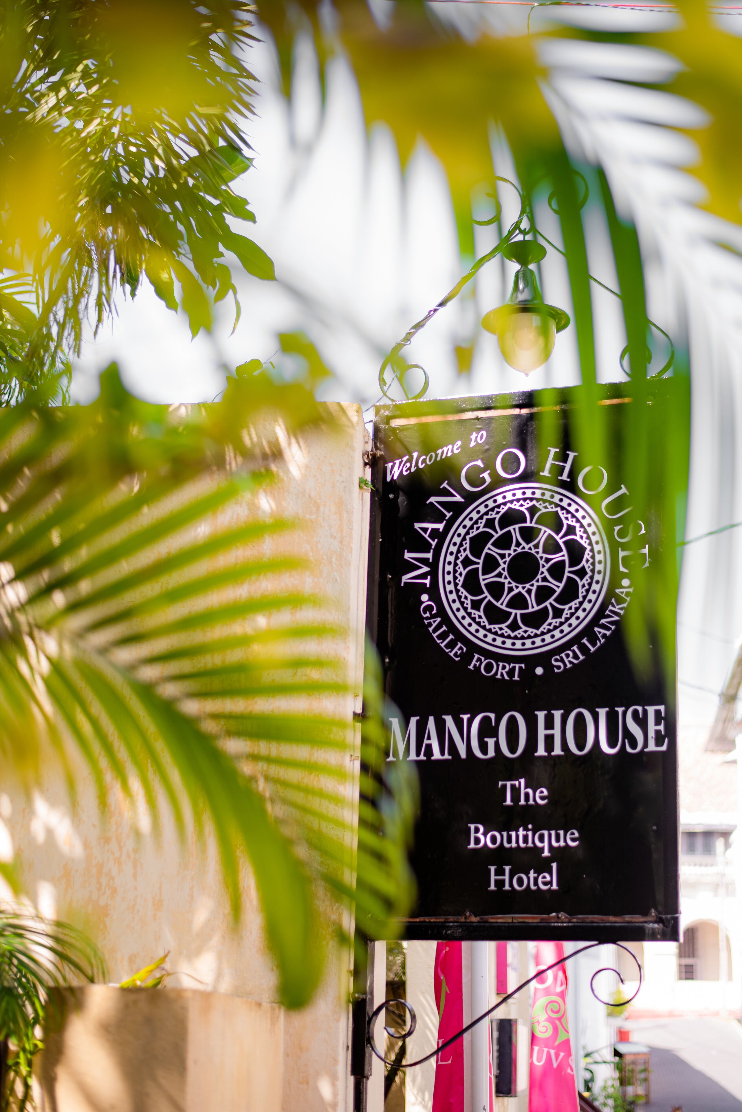 Señal de Mango House, un hotel boutique, con un mensaje de bienvenida y un emblema decorativo.