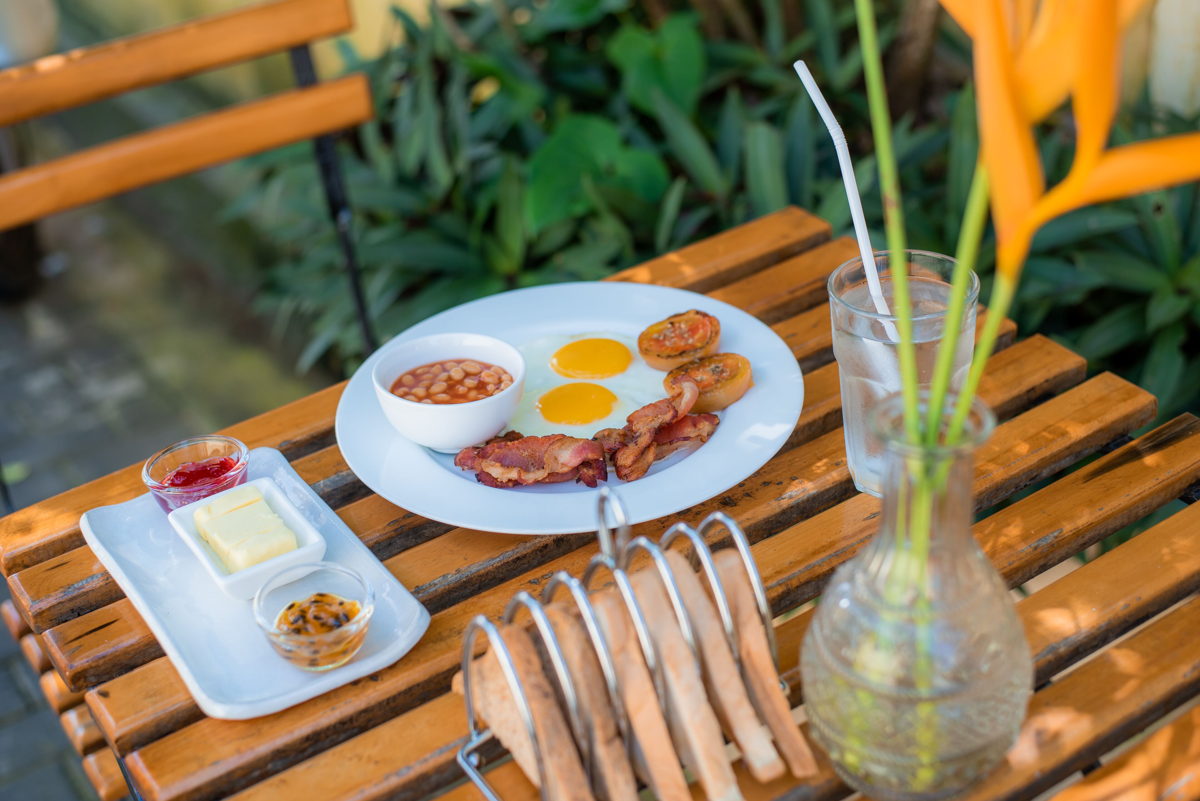 Un plato de desayuno con huevos, tocino, frijoles, mantequilla y mermelada sobre una mesa de madera.