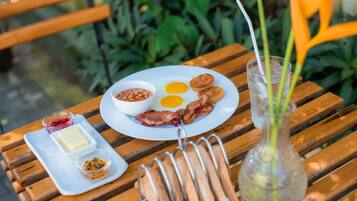 Un plato de desayuno con huevos, tocino, frijoles, mantequilla y mermelada sobre una mesa de madera.