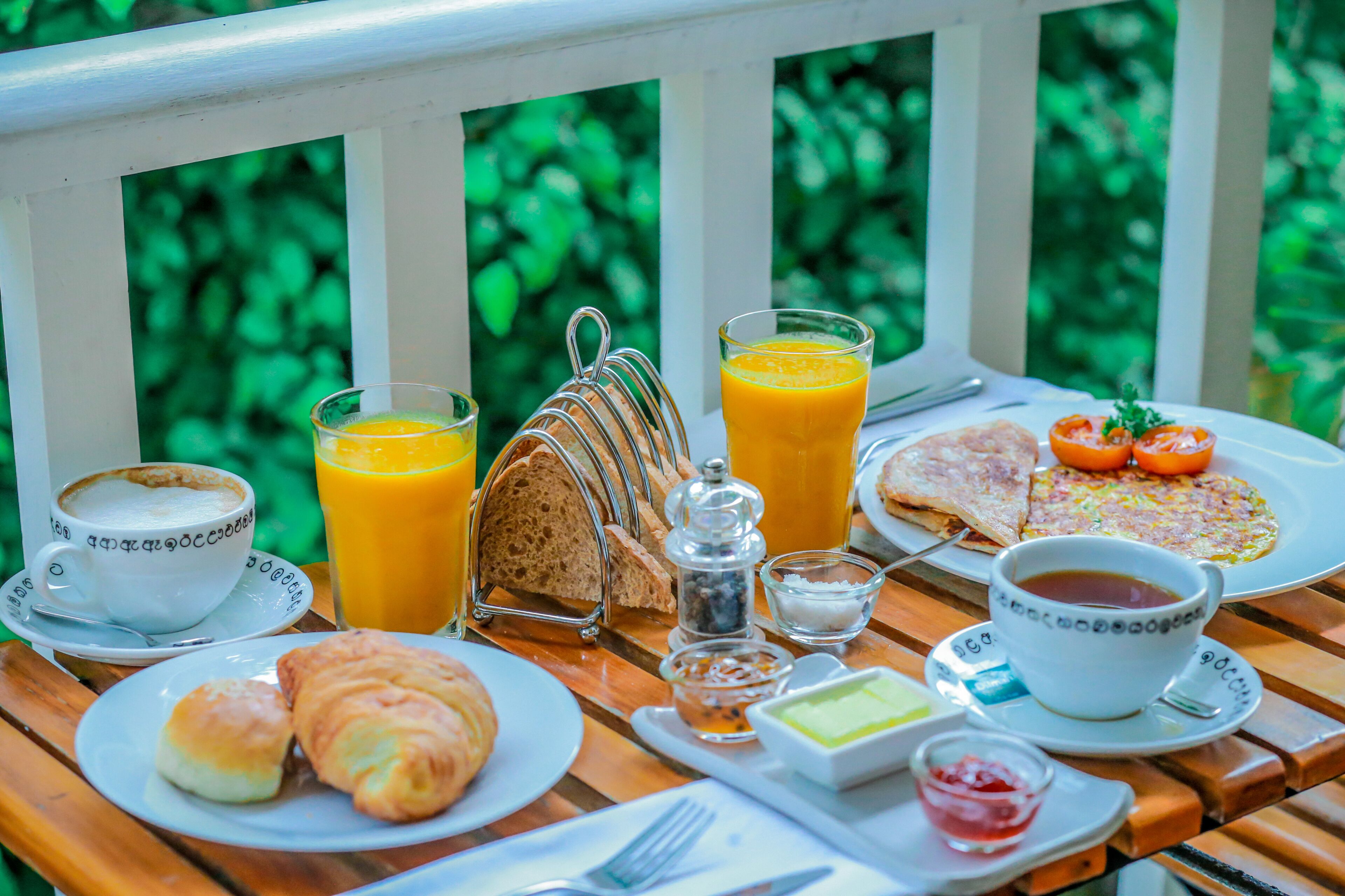 A breakfast table with croissants, orange juice, coffee, toast, a plate of eggs, tomatoes, and a cup of tea.