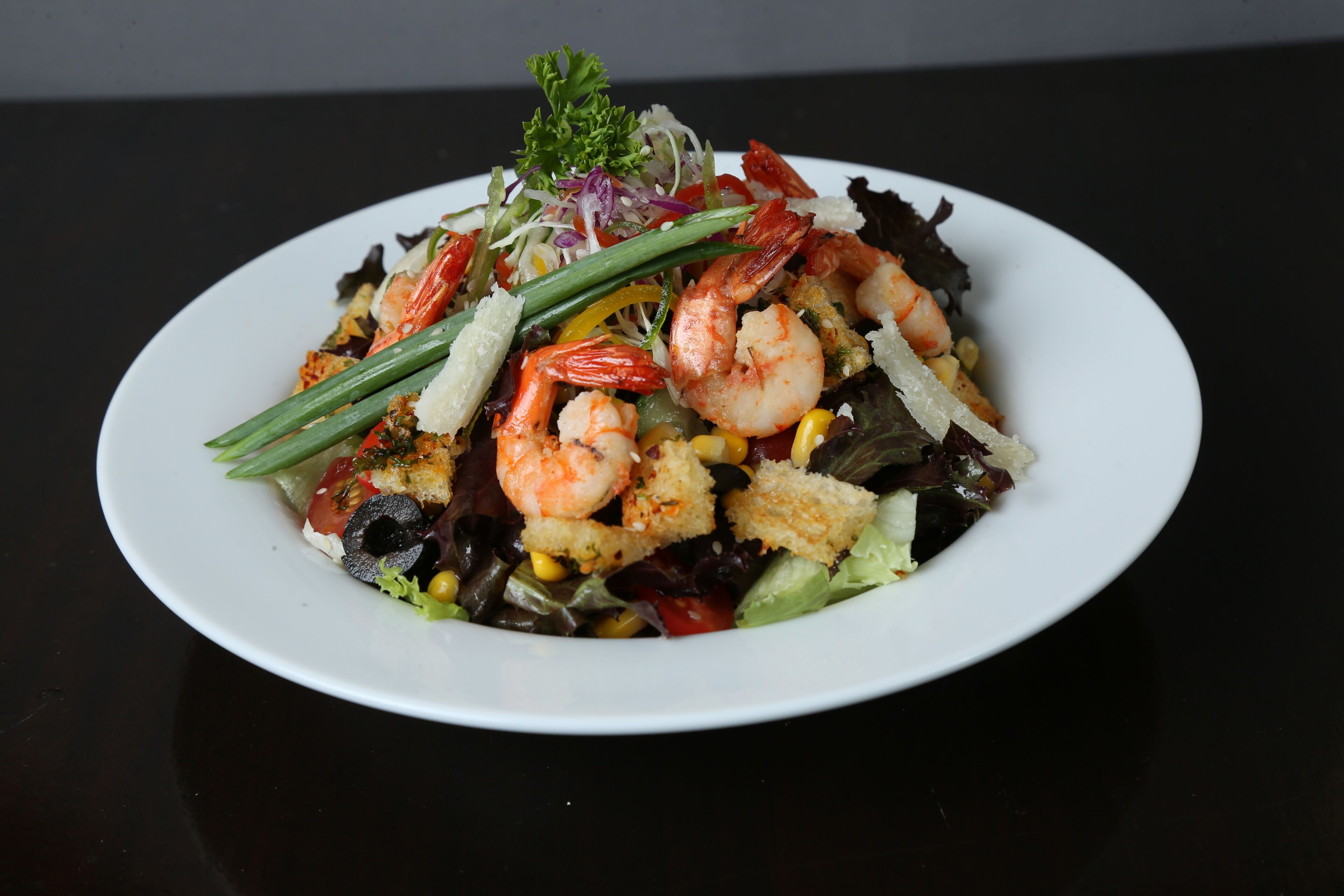 A plate of shrimp and vegetables on a black table.