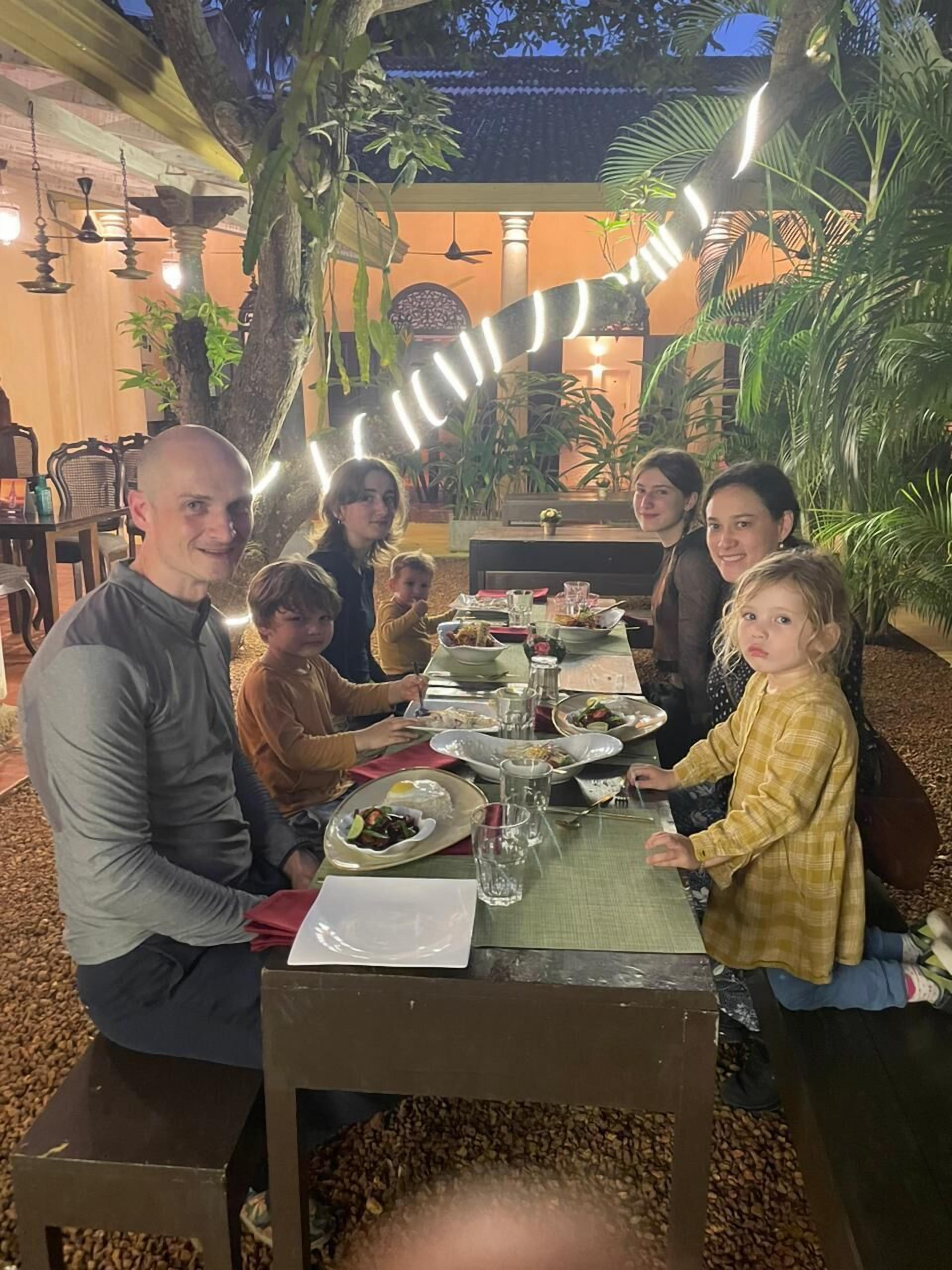 A family dining at an outdoor table with a variety of dishes, surrounded by greenery and traditional decor.
