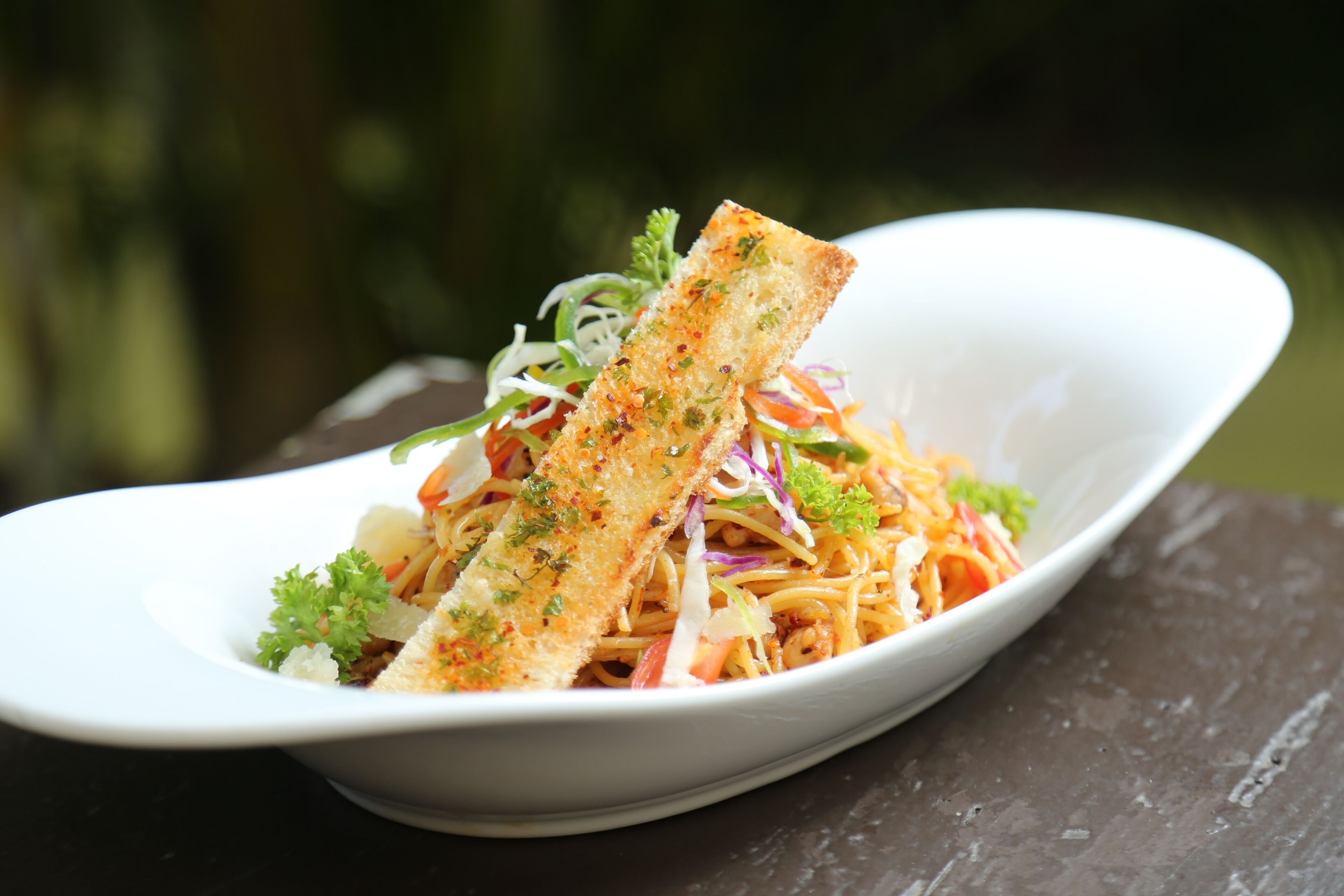 A white bowl with a salad and a piece of bread on a dark surface.