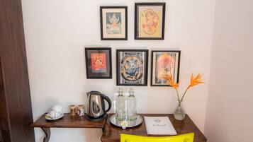 Una habitación con un escritorio de madera, una silla amarilla, obras de arte enmarcadas en la pared, una bandeja con vasos y una jarrera, y un cartel de bienvenida.