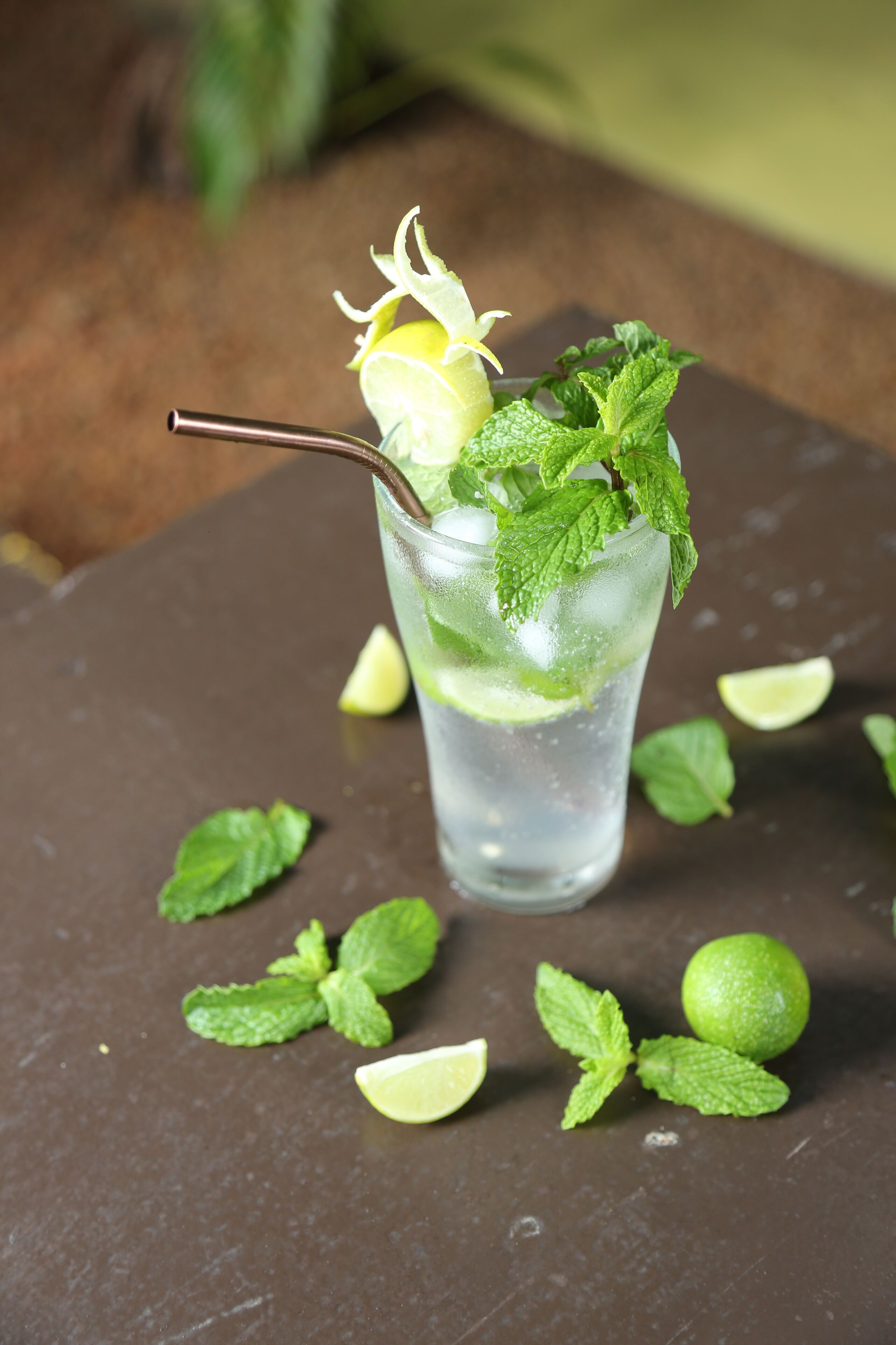 Ein Glas mit einem klaren Getränk, Minzblättern und Limettenscheiben auf einer dunklen Oberfläche mit verstreuten Limettenstücken.