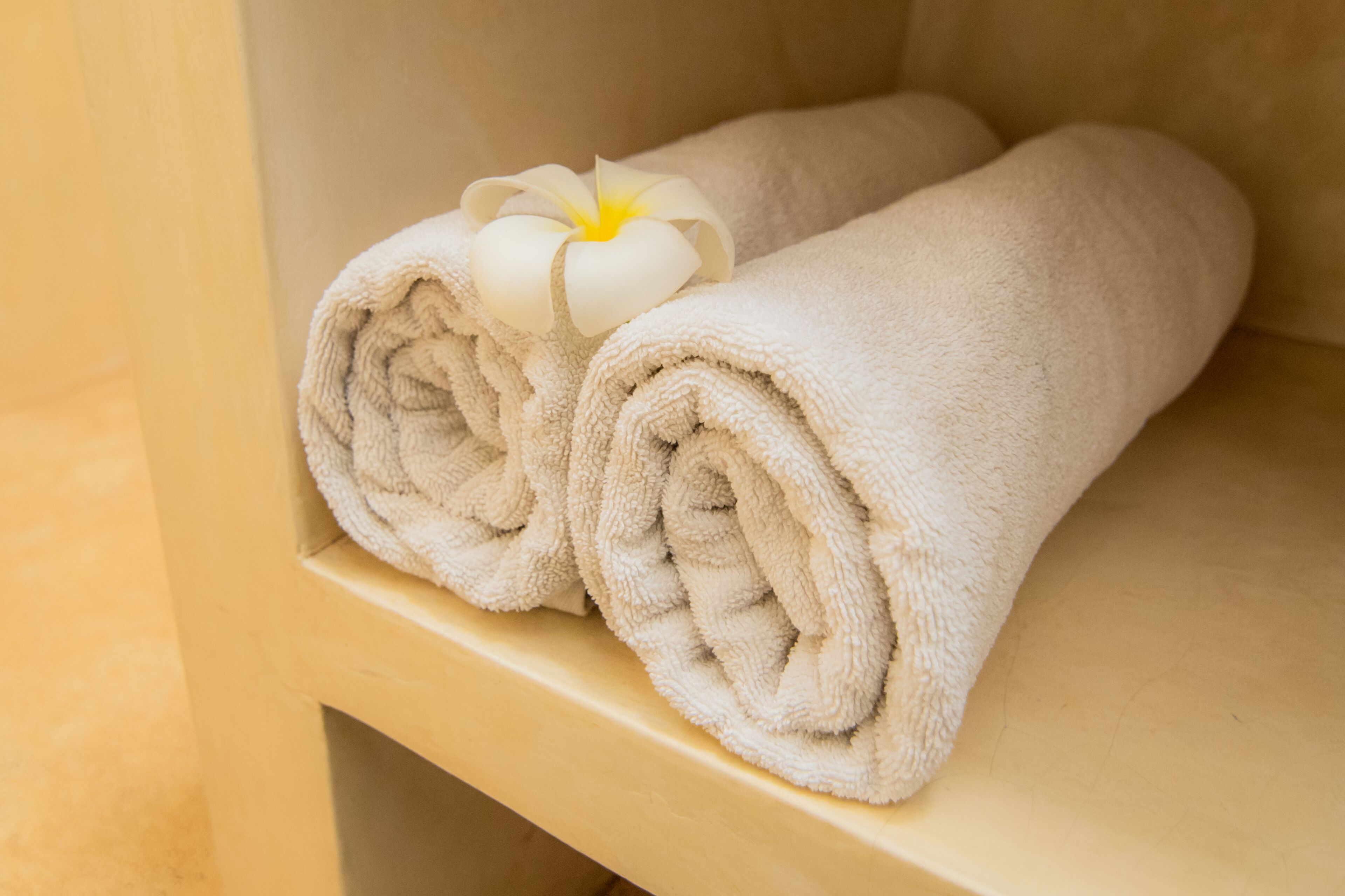 A neatly folded beige towel with a white flower on a wooden shelf.