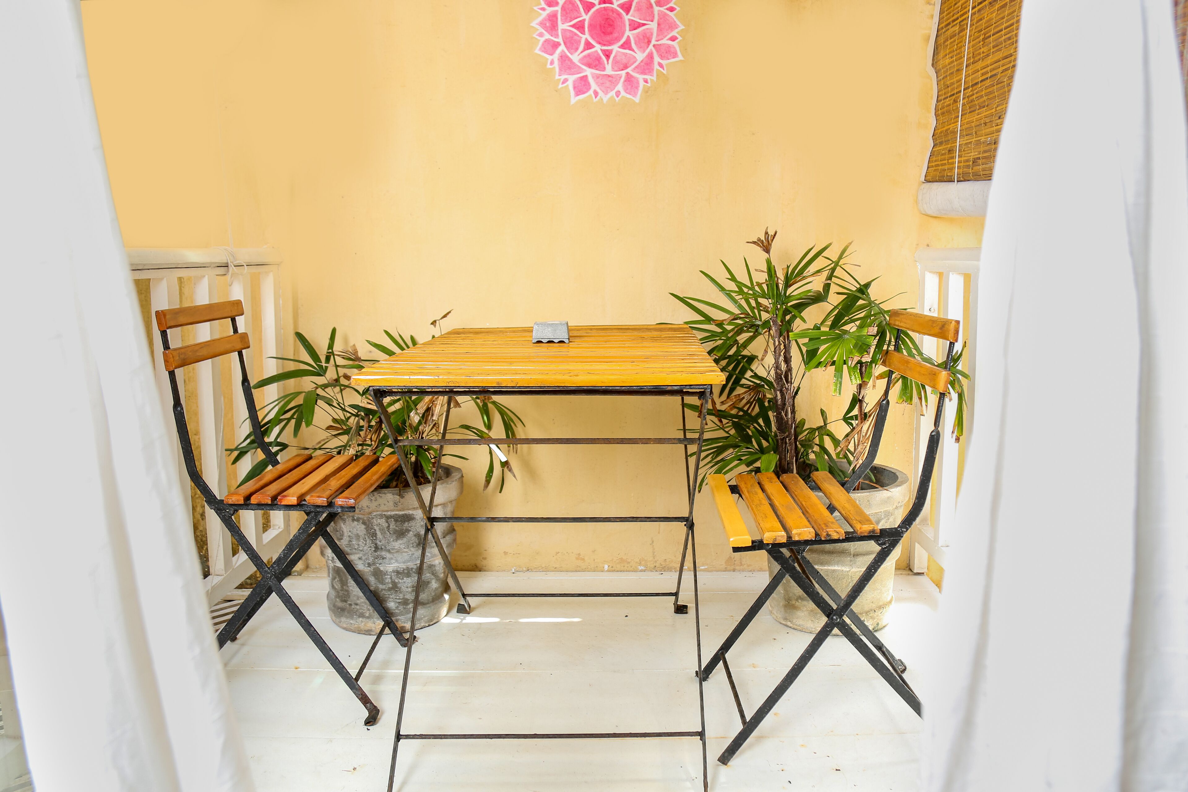 Un pequeño espacio al aire libre con una mesa y dos sillas, rodeado de plantas en macetas.