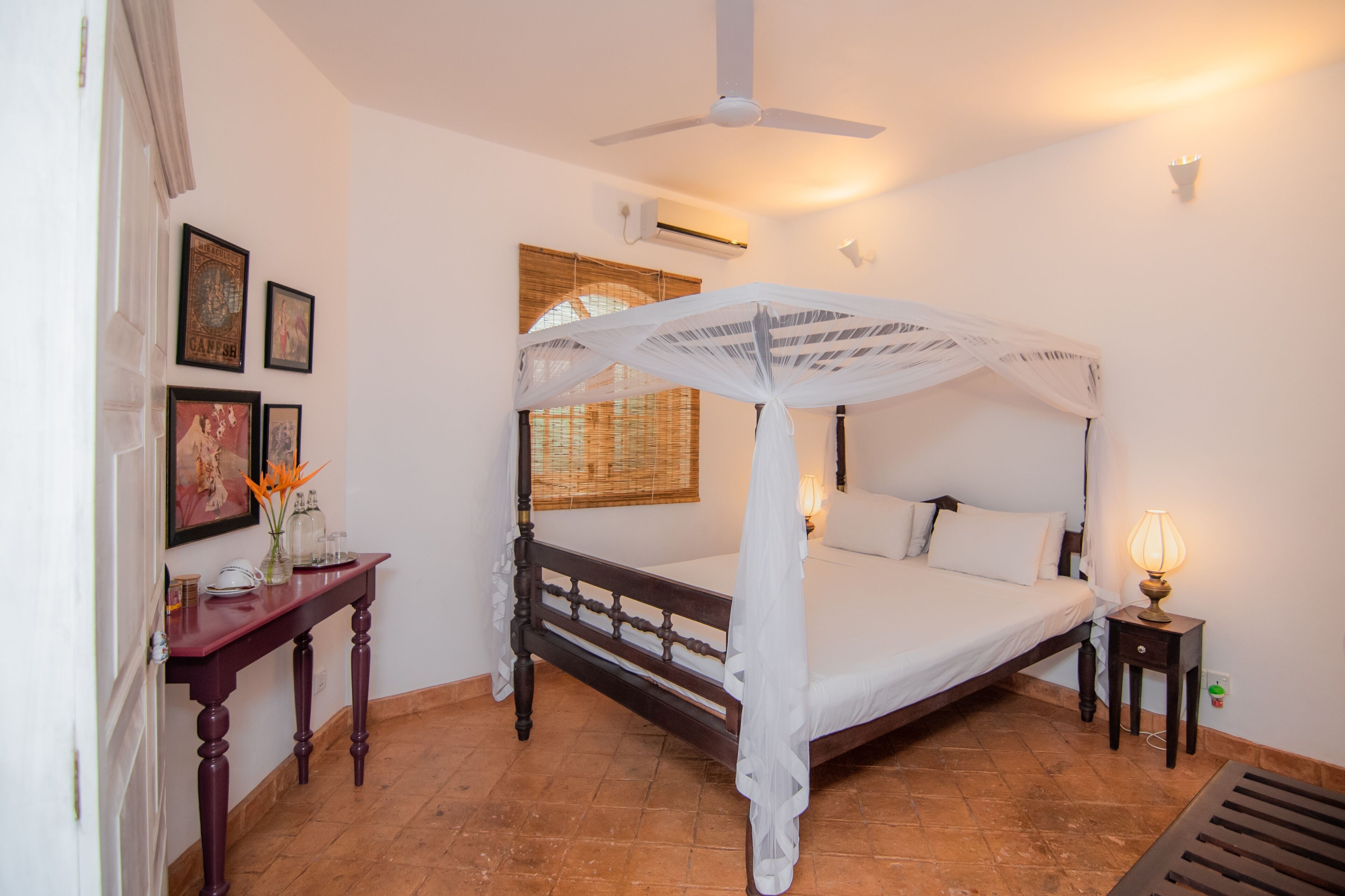 A bedroom with a four-poster bed, a bedside table, a lamp, and a ceiling fan.