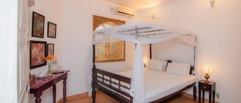 A bedroom with a four-poster bed, a bedside table, a lamp, and a ceiling fan.