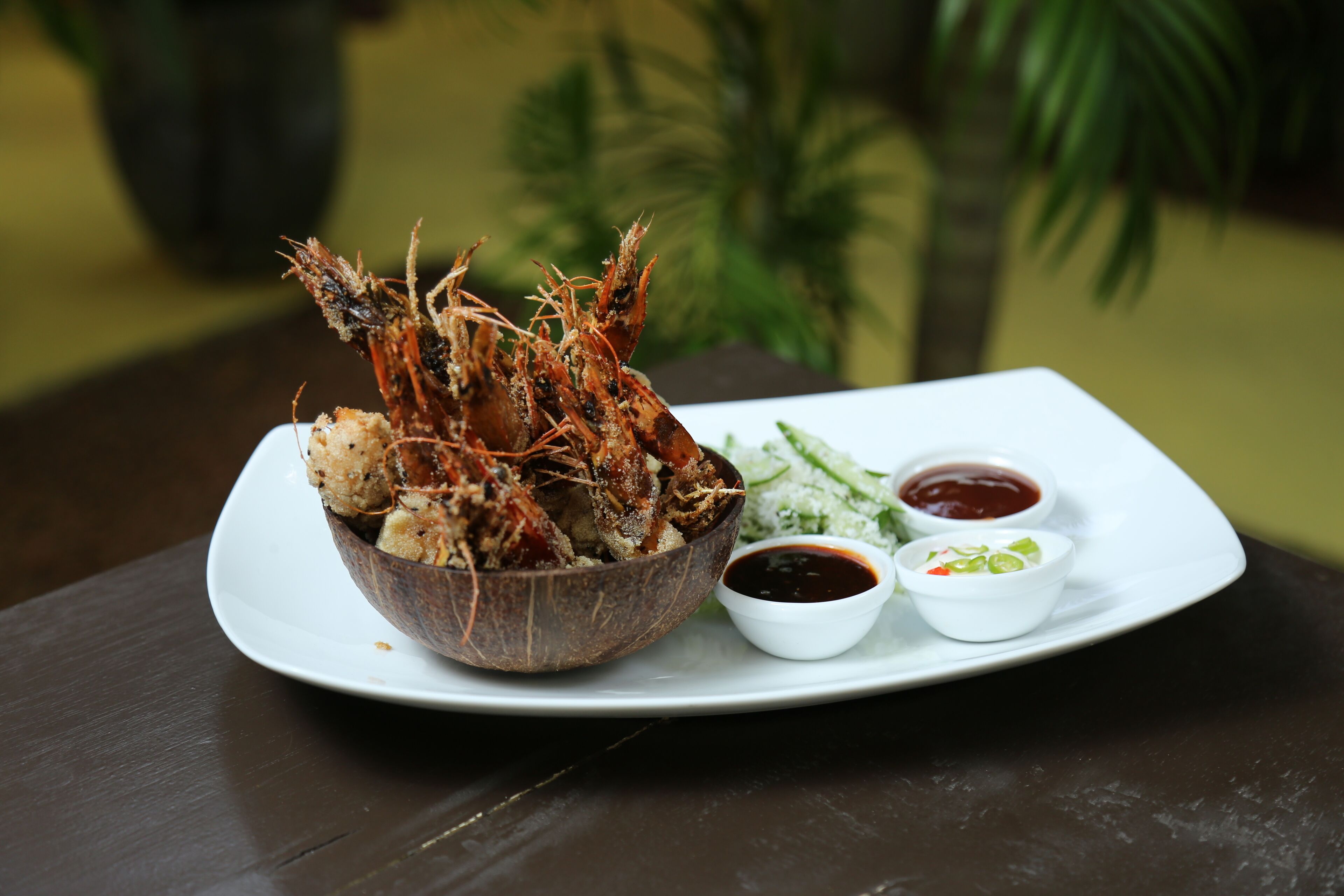Un plato con un bol de mariscos fritos, dos recipientes pequeños con salsas para mojar, y un plato blanco.