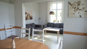 A modern living room with a wooden dining table, two grey sofas, a white chair, and a floor lamp. - Ronneby Brunnspark Vandrarhem och B&B - Hostel (Ronneby)