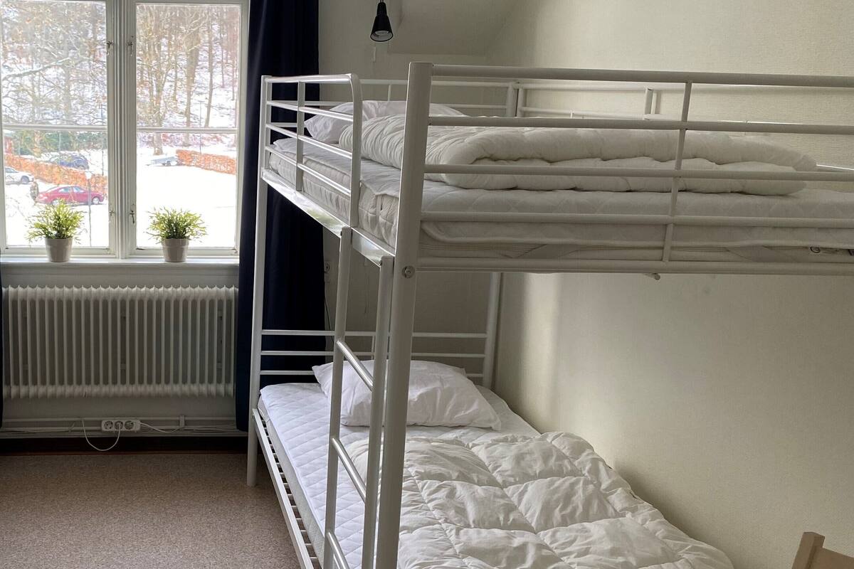 A bunk bed room with a window, radiator, and a small table.