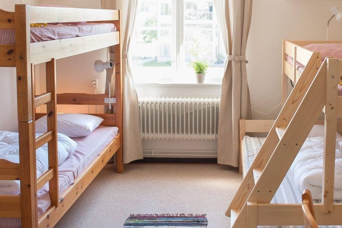 A room with bunk beds, a radiator, a window with curtains, and a small plant.