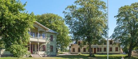 A two-story building with a balcony, surrounded by a grassy area and trees.