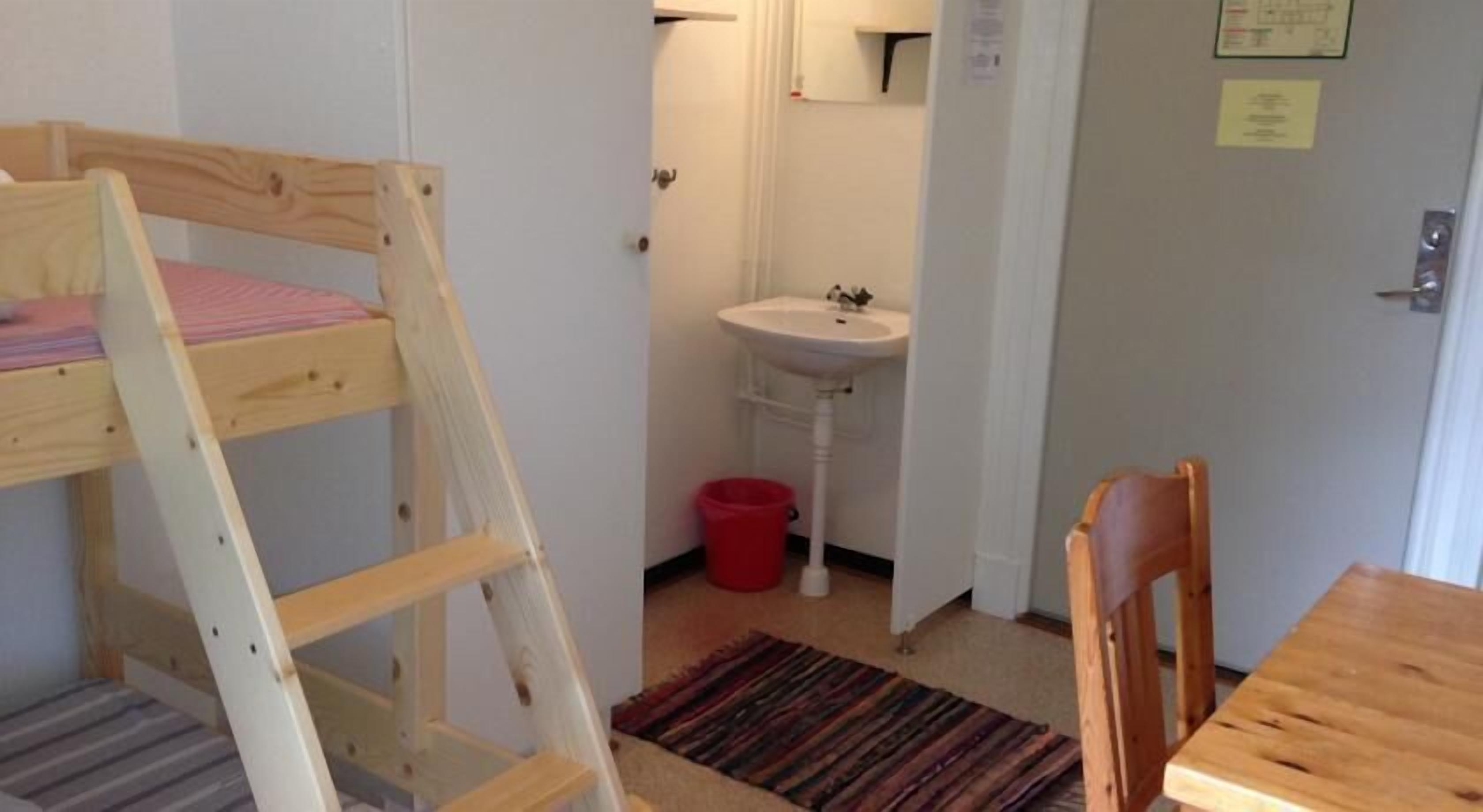 A bunk bed, a sink, a red bucket, a chair, and a table in a room.