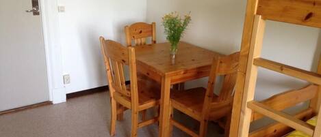 Una mesa de madera para comer con cuatro sillas, un jarrón pequeño con flores y una cama litera con colcha a rayas rosa y blanca.