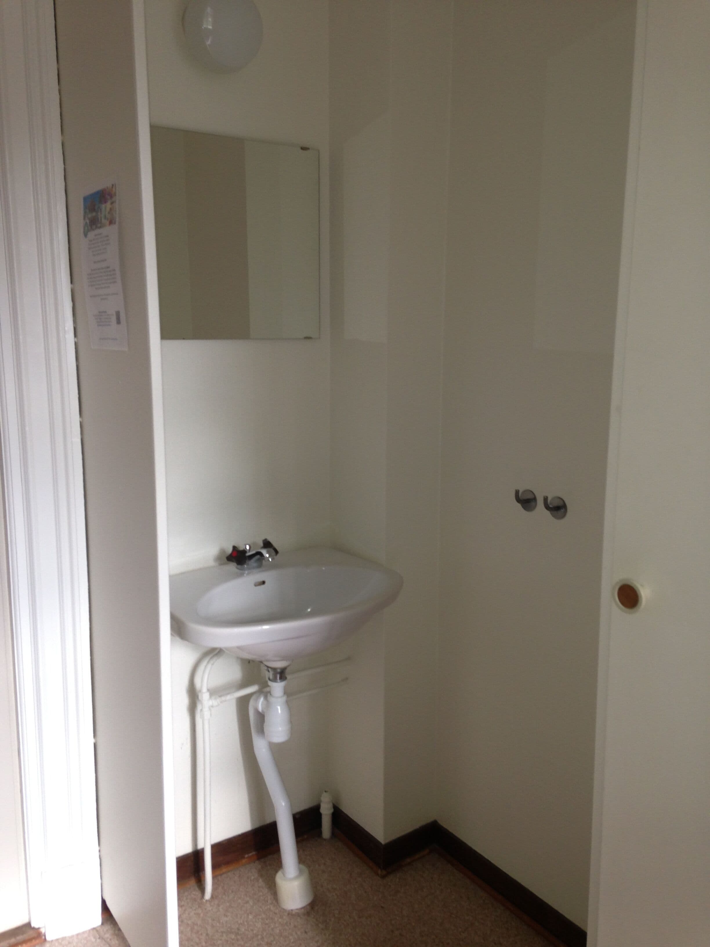 Un baño con un lavamanos blanco, un espejo encima y una puerta con dos pomos.