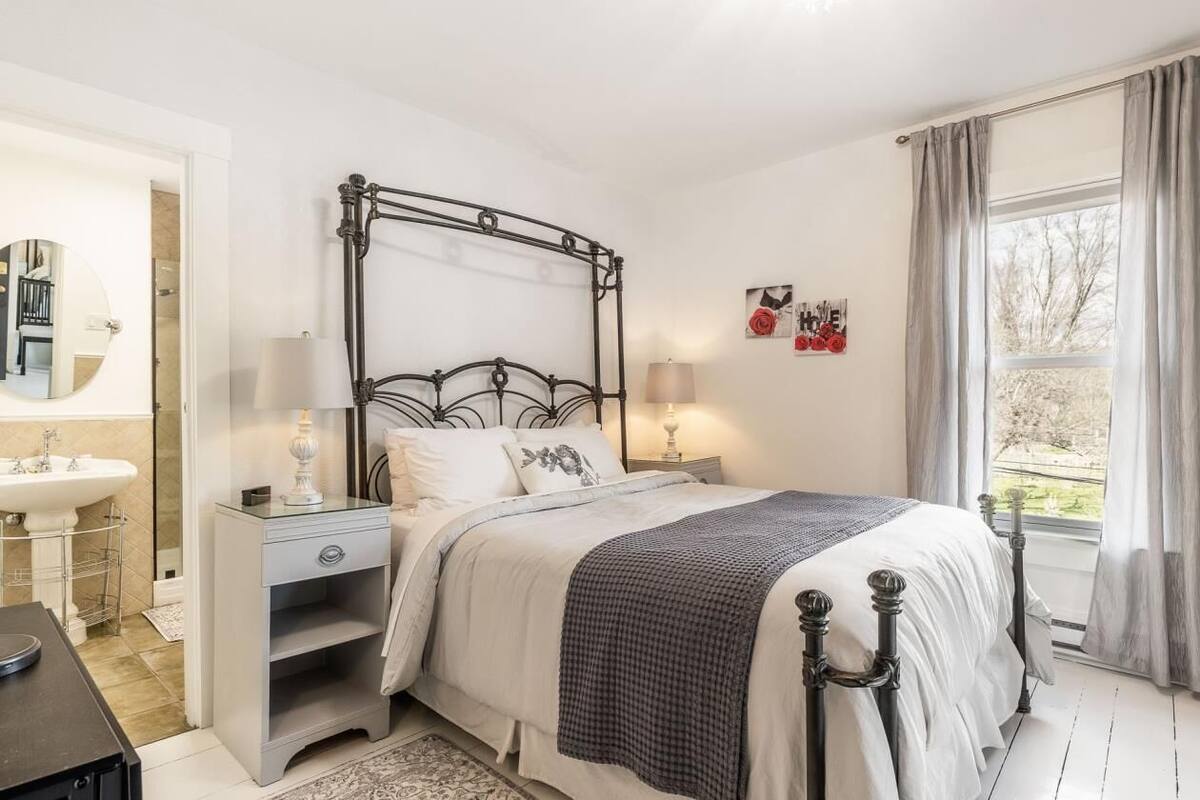 A bedroom with a four-poster bed, bedside tables, a nightstand, a mirror, and a window with curtains.