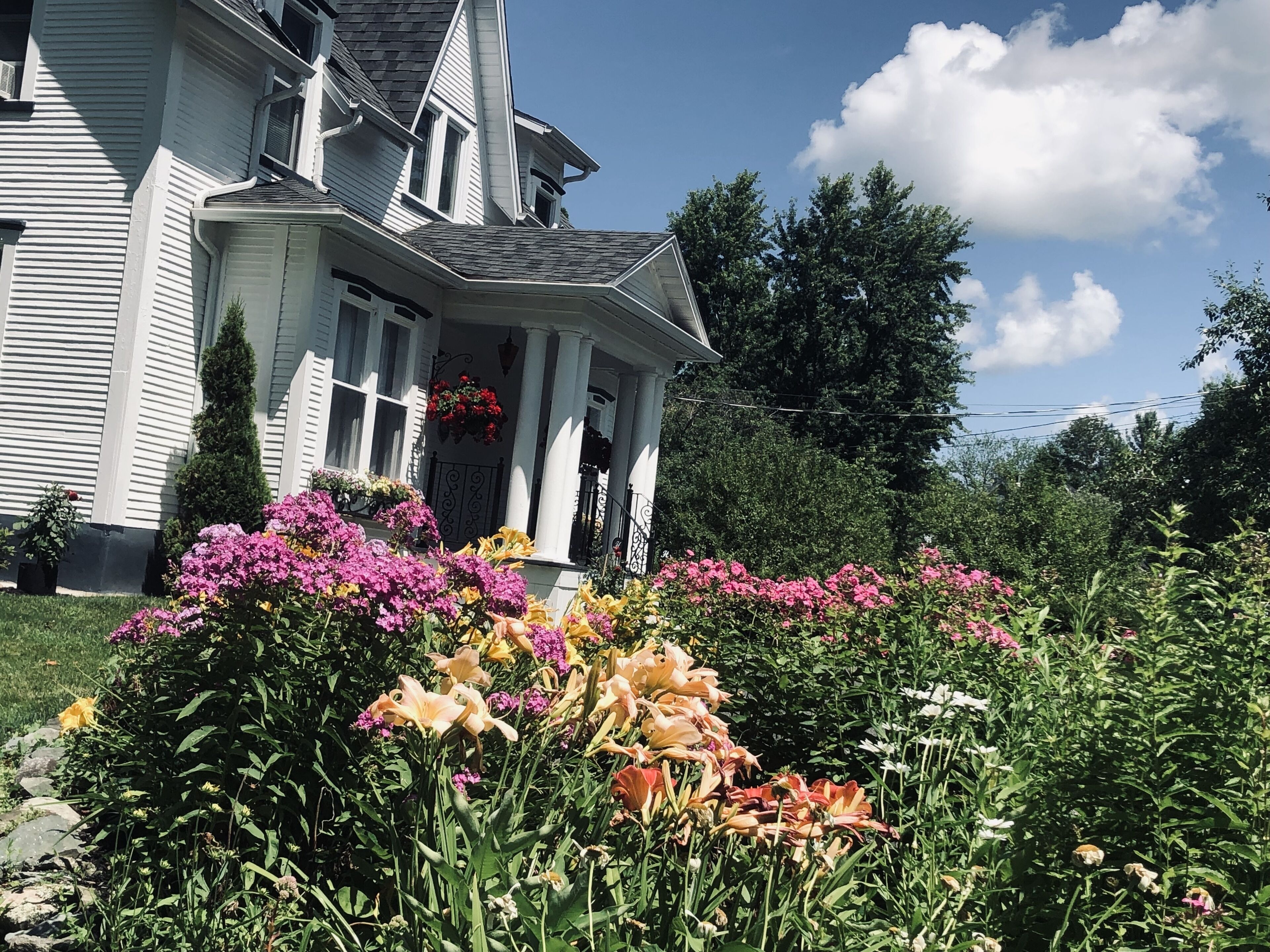 A two-story house with a porch, surrounded by a garden with various flowers and plants.