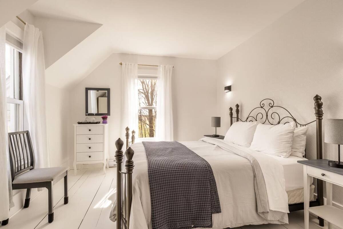 A bedroom with a bed, a chair, a dresser, a nightstand, and a window with curtains.