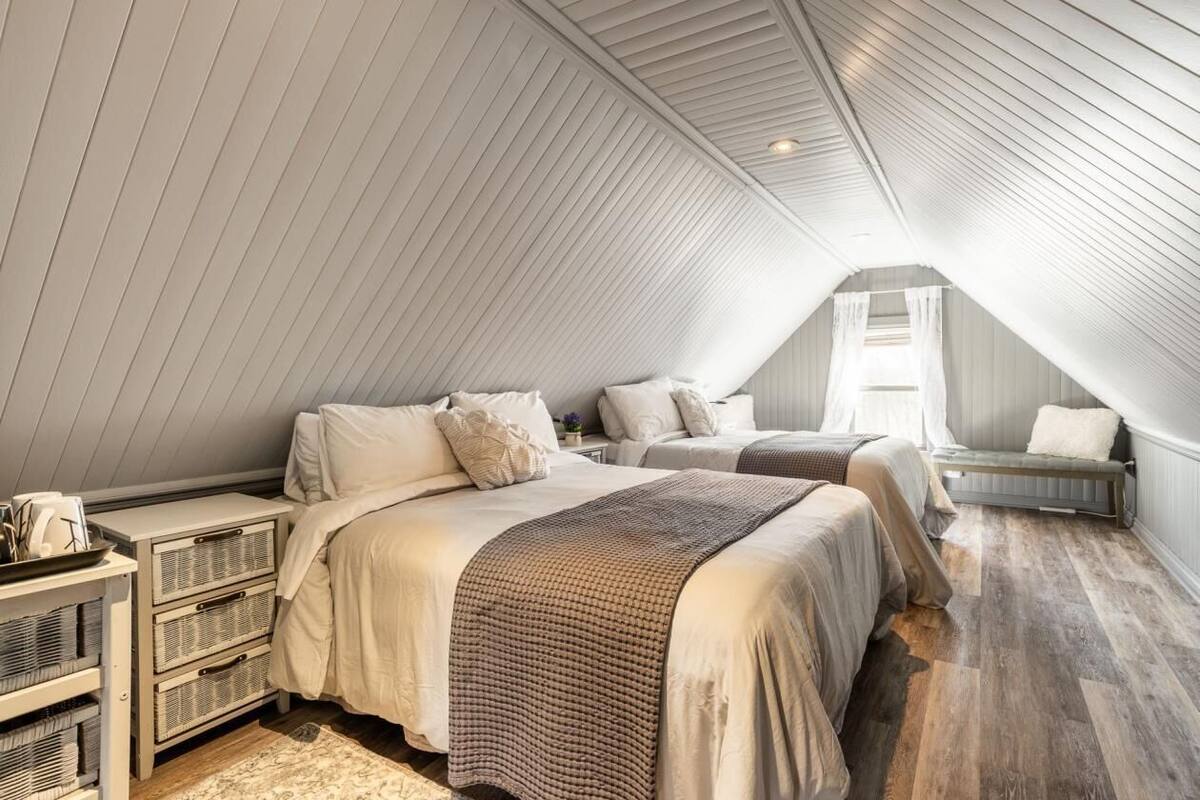 A cozy attic bedroom with two beds, a bench, and a small table with a basket.