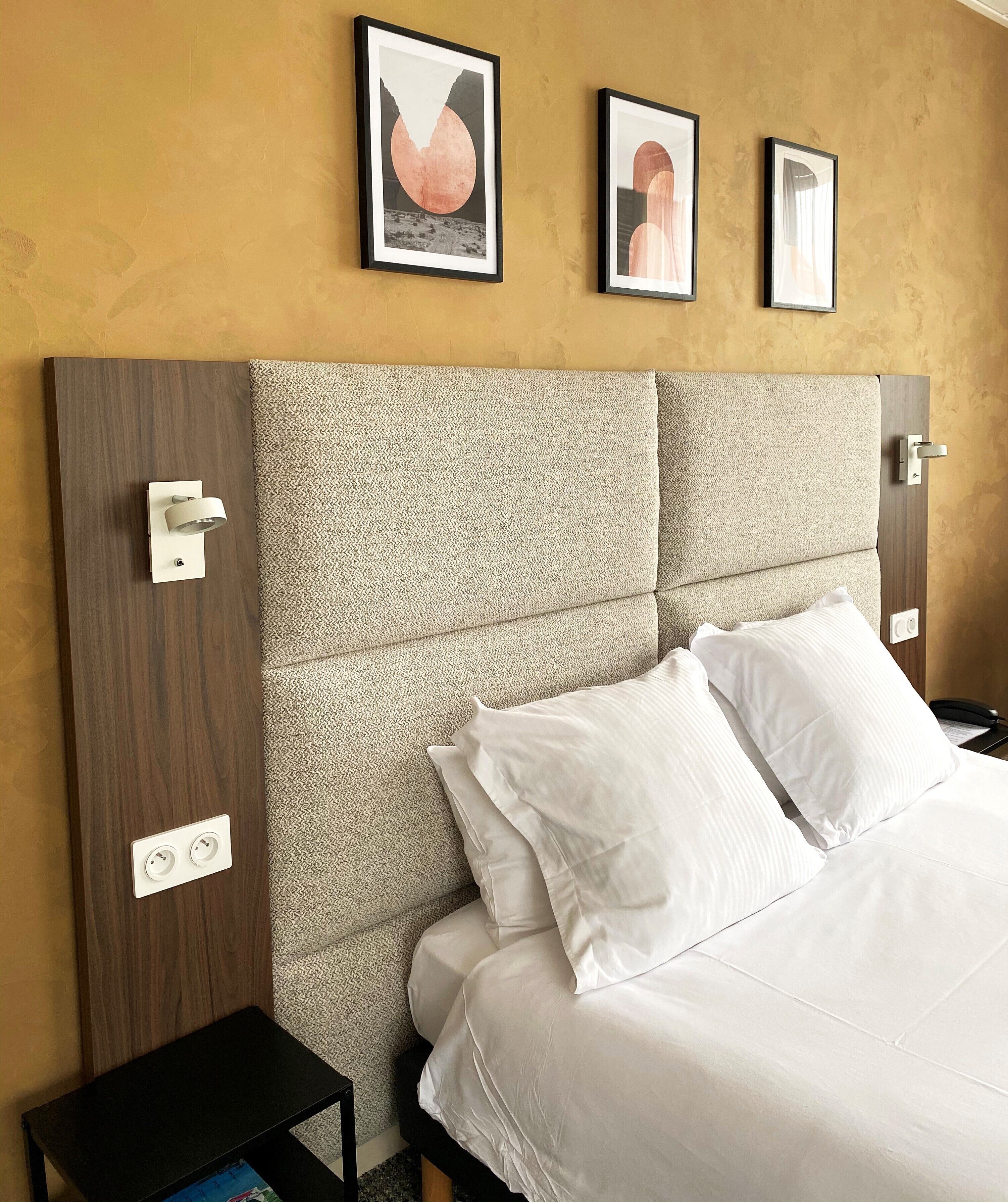 A hotel room with a large bed, a headboard with a textured pattern, two bedside tables, and three framed pictures on the wall.