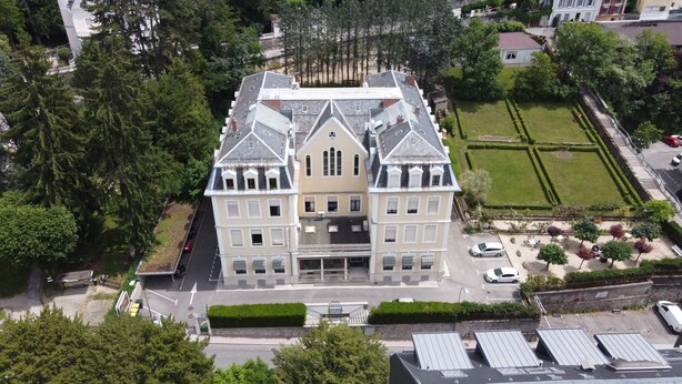 Un edificio grande de varios pisos con fachada simétrica, entrada central y un césped bien cuidado.