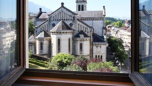 Vista de una iglesia histórica con una aguja alta, a través de una ventana con un jarrón de flores y un libro sobre una mesa.