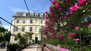 Un edificio con fachada simétrica, una entrada central y un jardín lleno de flores rosadas.