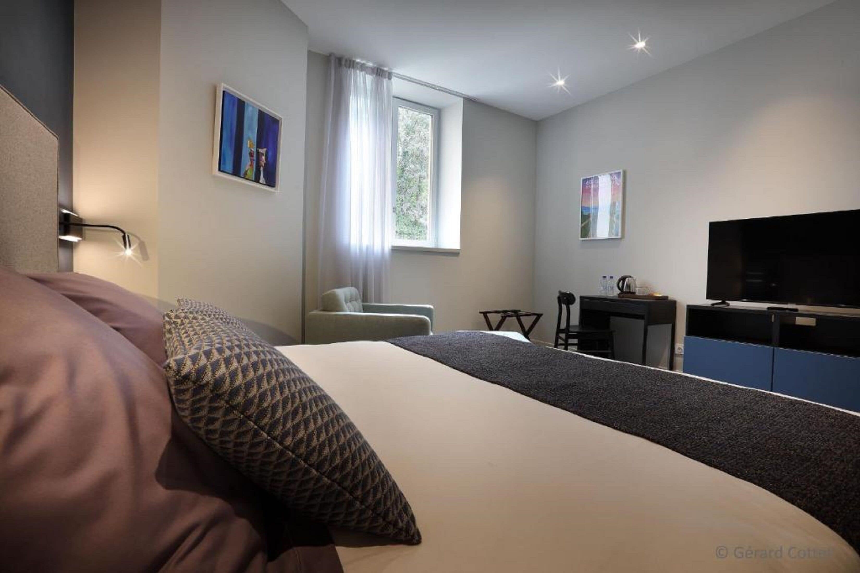 Moderni hotellihuone, jossa on suuri sänky, työpöytä, tuoli, televisio ja ikkuna, jossa on verhot.