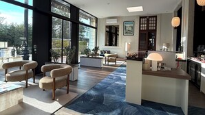 Amplia sala de estar con ventanas grandes, una zona de estar central con sofás y sillones, un área de cocina y un tapete azul con estampado.