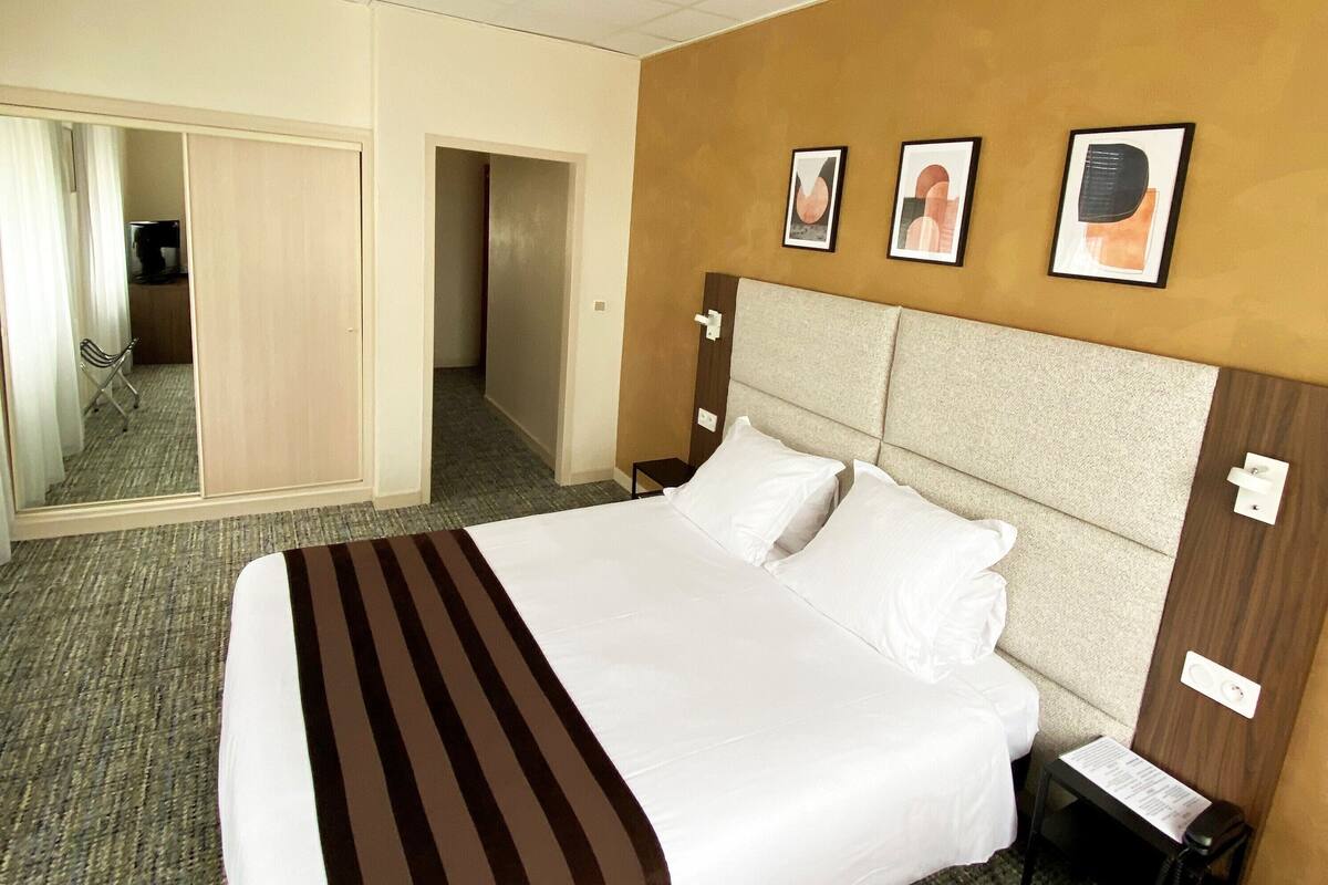 Een hotelkamer met een groot bed, nachtkastje, spiegel en een deur naar een gang.