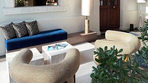 Una sala de estar moderna con un sofá azul, sillas de mimbre, una mesa de centro y un ventanal grande.