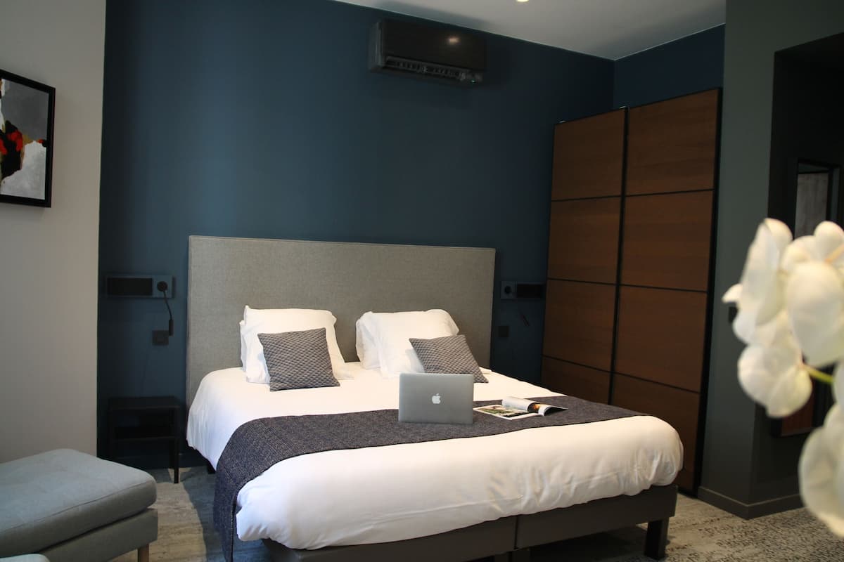 Een moderne slaapkamer met een groot bed, een laptop op het bed en uitzicht op een stadslandschap door het raam.