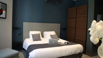 A modern bedroom with a large bed, a laptop on the bed, and a view of a cityscape through the window.