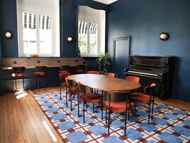 A room with a wooden table, orange chairs, a piano, and a patterned rug.