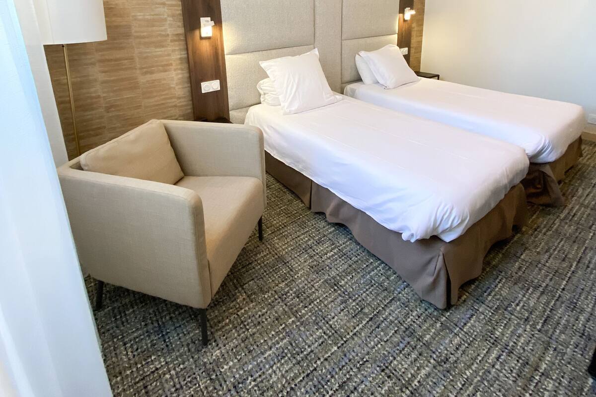 Een hotelkamer met twee bedden, een stoel en een lamp.