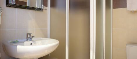 A bathroom with a white sink, a mirror, a shower enclosure, and a toilet.