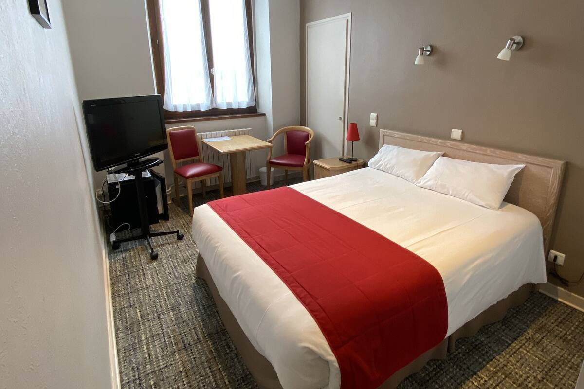 Een hotelkamer met een bed, een bureau, een stoel, een televisie en een raam.