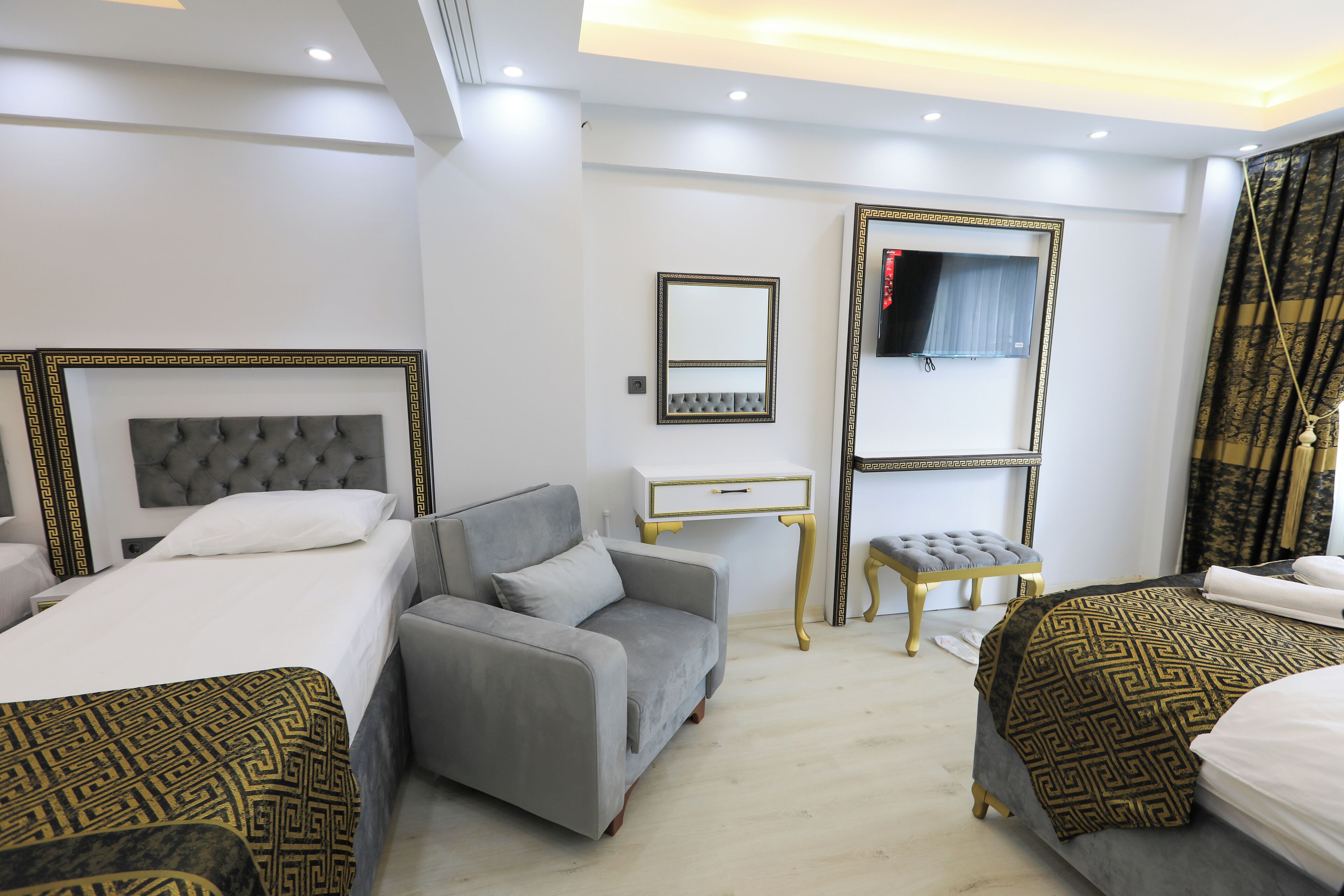 A hotel room with two beds, a grey sofa, a small table, and a TV.