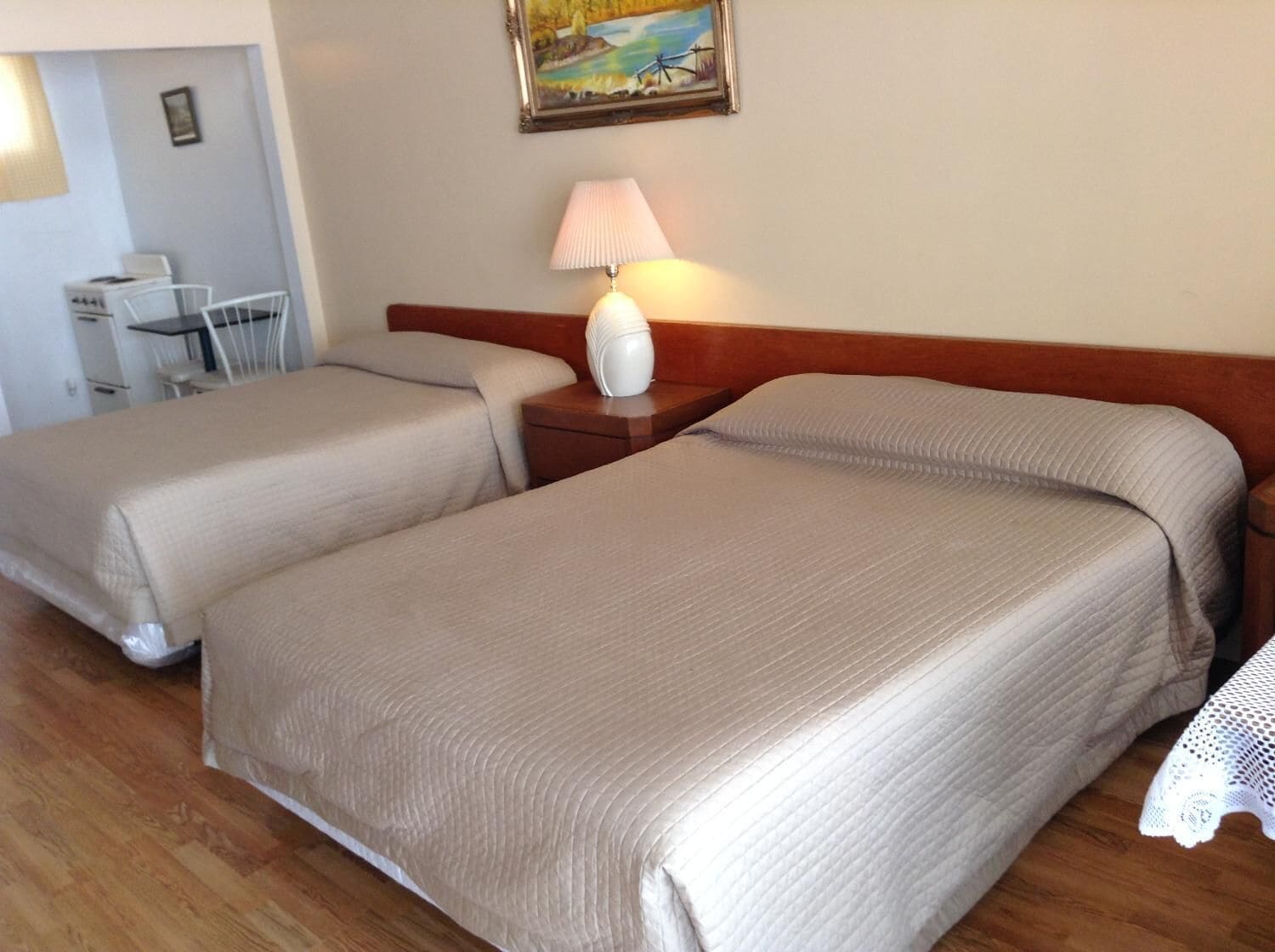 Une chambre d’hôtel avec deux lits simples, une tête de lit en bois, une table de chevet avec une lampe et un petit bureau avec une chaise.