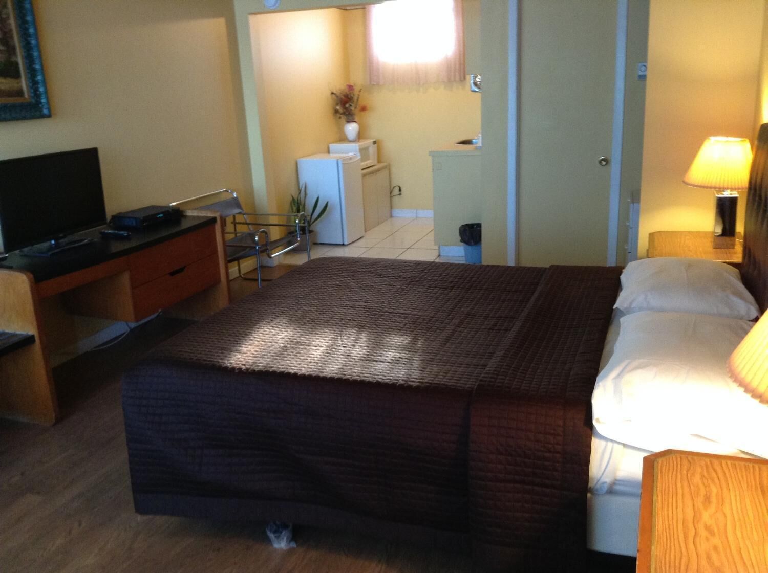 Una habitación de hotel con cama, escritorio con televisor, kitchenette pequeña y baño.