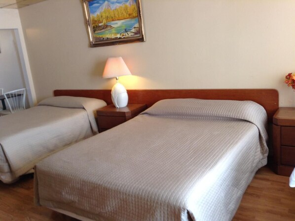 Una habitación de hotel con dos camas, una mesita de noche con lámpara y un cuadro en la pared.